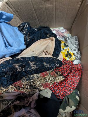 une boîte en carton remplie de vêtements, ainsi que des vêtements éparpillés par terre