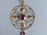 a close up of a gold pendant with a red stone on it