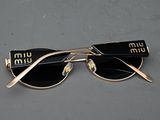 gold rimmed sunglasses with black lenses on a gray surface