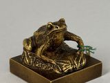 bronze figurine of a frog sitting on a piece of wood with a flower in its mouth