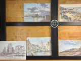 quatre tableaux posés sur une étagère, devant laquelle se trouve une horloge