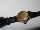 a gold watch on a black leather strap on a white surface