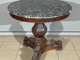une table ancienne au plateau en marbre et au piètement en bois, posée sur un sol carrelé