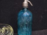 a blue glass bottle with a silver top next to a glass bowl