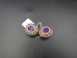 une paire de boucles d'oreilles violettes et dorées posées sur un fond noir