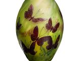 un vase vert orné de papillons, posé sur un fond blanc