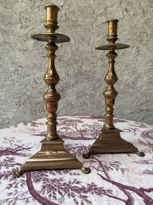 pair of brass candlesticks on a table with a purple and white floral tablecloth