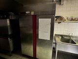 une cuisine faiblement éclairée, équipée d'appareils électroménagers en inox et d'un évier