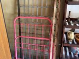 a pink bed with a metal frame next to a wooden shelf