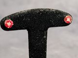 une paire de boucles d'oreilles à clous ornées de fleurs rouges et blanches, posées sur un socle noir