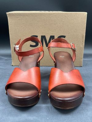 une paire de sandales marron et orange, avec une boîte en arrière-plan