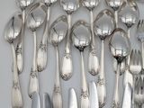 a lot of silver spoons and knives on the table