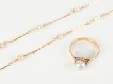 two gold rings and a pearl necklace on a white surface