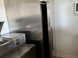 un grand réfrigérateur en acier inoxydable dans une cuisine où est accrochée une horloge au mur