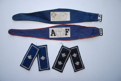 un ensemble composé de trois insignes militaires et d'une ceinture, posé sur un fond blanc