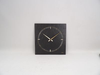 une horloge noire aux aiguilles dorées accrochée à un mur blanc