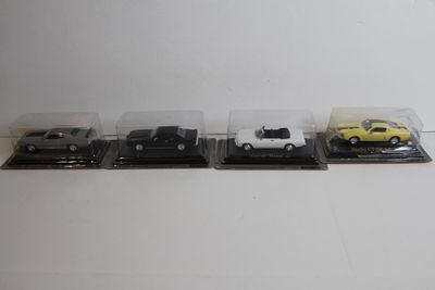 quatre modèles réduits de voitures dans des boîtes en plastique, posés sur une surface blanche