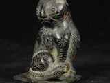 statue d'un chat tenant un poisson entre ses pattes, sur fond noir
