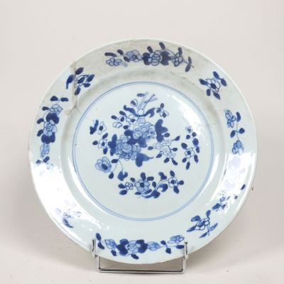 assiette bleue et blanche ornée de fleurs et de feuilles, posée sur un socle