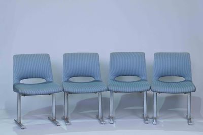 four blue chairs sitting in a row against a white wall