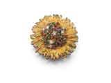 a close up of a gold brooch with colorful stones on a white surface