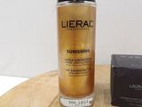 lieracc sunissme face and body lotion in a glass bottle next to a black box on a wooden table
