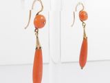 pair of orange coral and gold earrings on clear acrylic stand