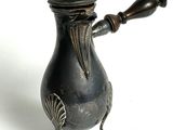 une petite théière en métal avec une poignée en bois, posée sur une surface blanche