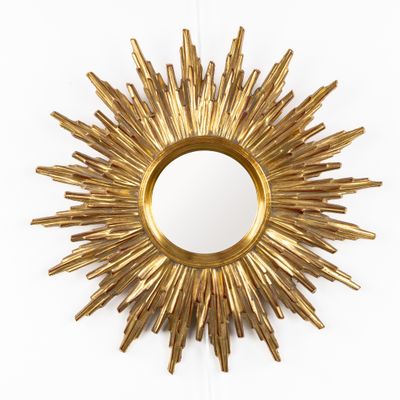 miroir doré à rayons de soleil sur un mur blanc, avec un fond blanc