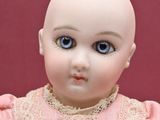 a small doll with blue eyes and a pink dress
