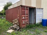 a red shipping container sitting in the grass next to a building