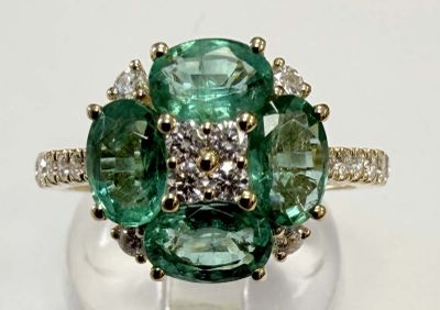 une photo d'une bague en diamant verte et blanche posée sur une surface blanche