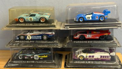 six modèles réduits de voitures différents, exposés dans une vitrine posée sur une table