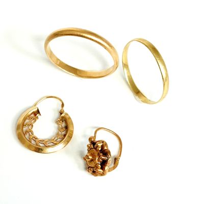 trois paires de bagues en or et une paire de boucles d'oreilles posées sur une surface blanche