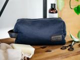 une trousse de toilette bleu marine avec une étiquette en cuir et une paire de ciseaux posée sur une table en bois