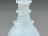 a white glass vase with a gold top on a table