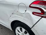 the rear end of a white car with a dent in it ' s bumper