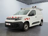La camionnette blanche est garée dans une grande pièce ; elle porte une bande rouge et blanche sur le côté.