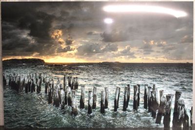 tableau représentant un coucher de soleil sur un plan d'eau d'où émergent des poteaux en bois
