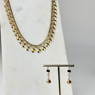 un ensemble composé d'un collier et de boucles d'oreilles en or, posé sur un socle en marbre