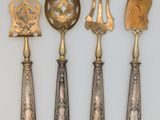 five antique spoons and a spatula are lined up on a white surface
