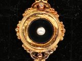une image représentant une broche noire et dorée ornée d'une perle