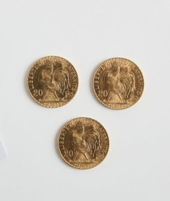 Trois pièces d'or sont représentées sur une surface blanche, à côté d'une paire de ciseaux
