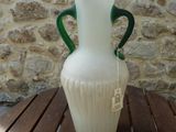 a white vase with green handles sitting on a wooden table