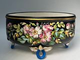 a black bowl with flowers painted on it on a stand