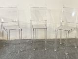 three clear plastic chairs sitting next to each other against a white wall