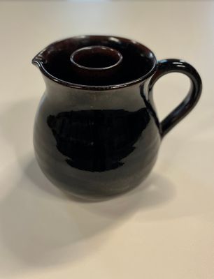 un pichet noir posé sur une table blanche, avec un couvercle marron
