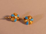 une paire de boucles d'oreilles en forme de fleurs aux teintes bleues et dorées sur un fond beige