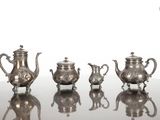 cinq théières en argent posées sur une table en verre