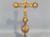 une croix dorée posée sur une table blanche, sur fond gris